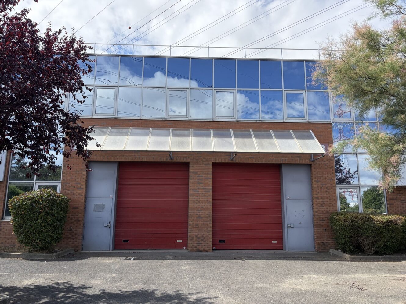 Bâtiment en briques doté de deux grandes portes de garage rouges, de fenêtres vitrées à l'étage supérieur et d'arbres de chaque côté.
