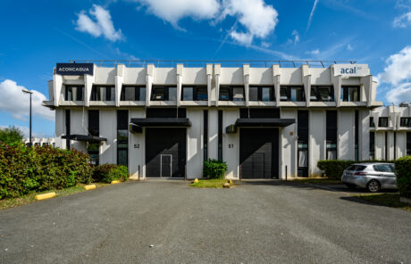 Un bâtiment commercial moderne avec une façade noire et blanche, étiqueté Aconcagua et acal, avec des entrées numérotées 51 et 52, et un petit parking devant.
