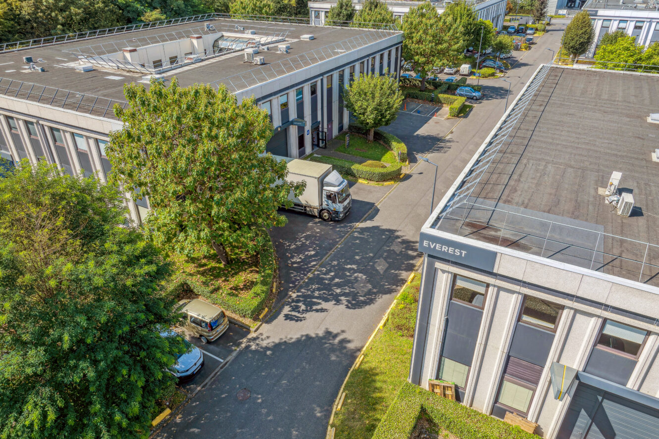 Vue aérienne d'immeubles de bureaux avec des voitures garées, des arbres et un camion sur une route, avec un bâtiment étiqueté EVEREST.