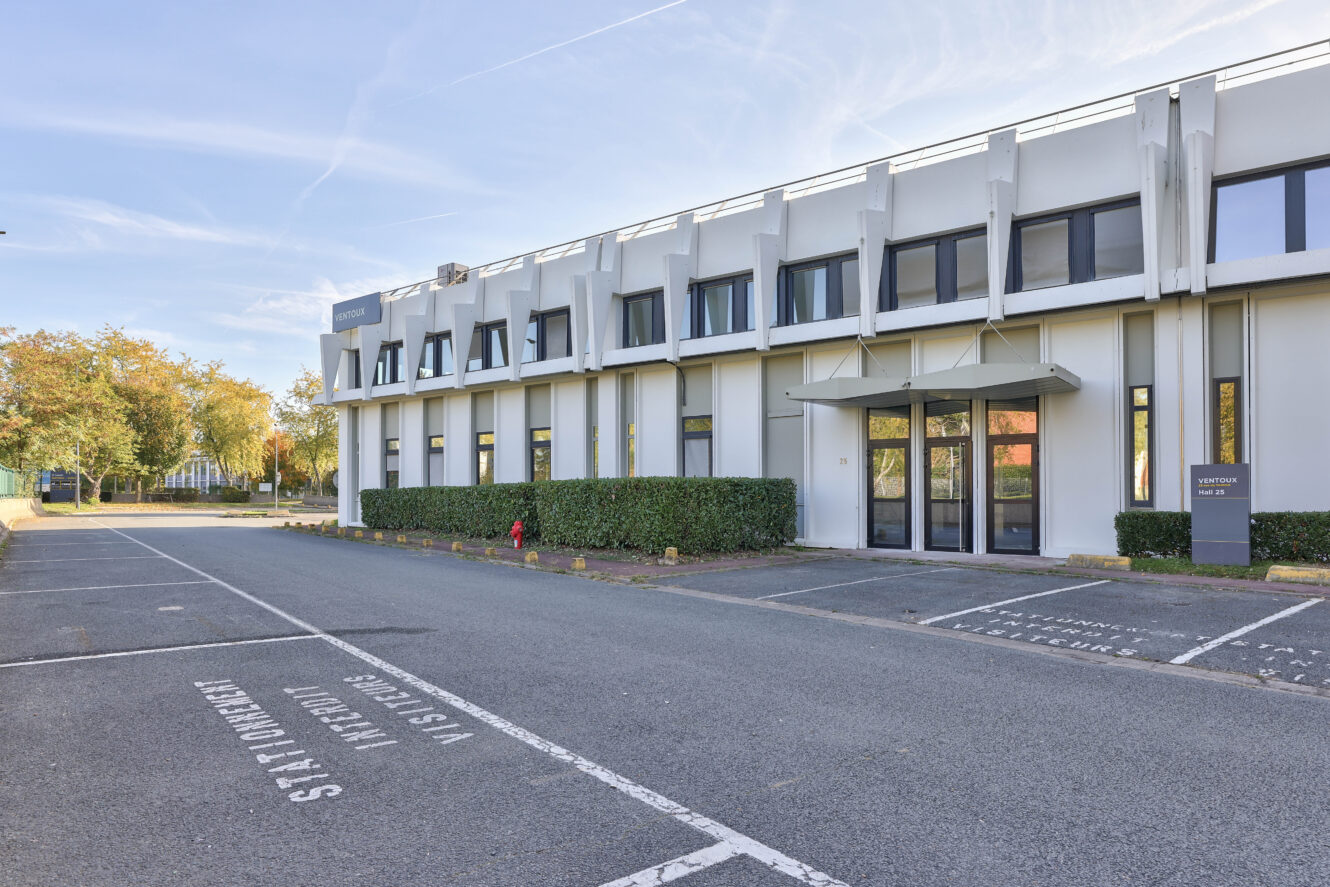 Un bâtiment commercial moderne de deux étages avec de grandes fenêtres, adjacent à un parking vide marqué de places réservées, par temps clair.