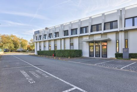 Un bâtiment commercial moderne de deux étages avec de grandes fenêtres, adjacent à un parking vide marqué de places réservées, par temps clair.