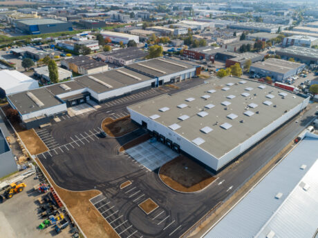 Vue aérienne d'un grand complexe d'entrepôts industriels avec les parkings adjacents, les quais de chargement et les bâtiments industriels environnants.