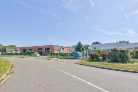 Une rue tranquille s'incurve devant un bâtiment scolaire clôturé aux murs colorés et à la verdure sous un ciel bleu limpide.