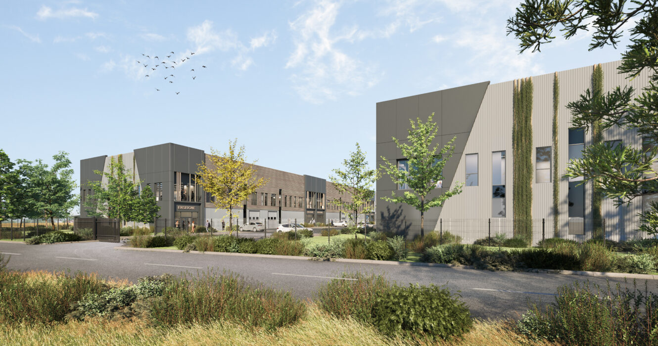 Immeubles de bureaux modernes aux façades géométriques entourés de verdure, d'arbres et d'une route au premier plan sous un ciel partiellement nuageux.