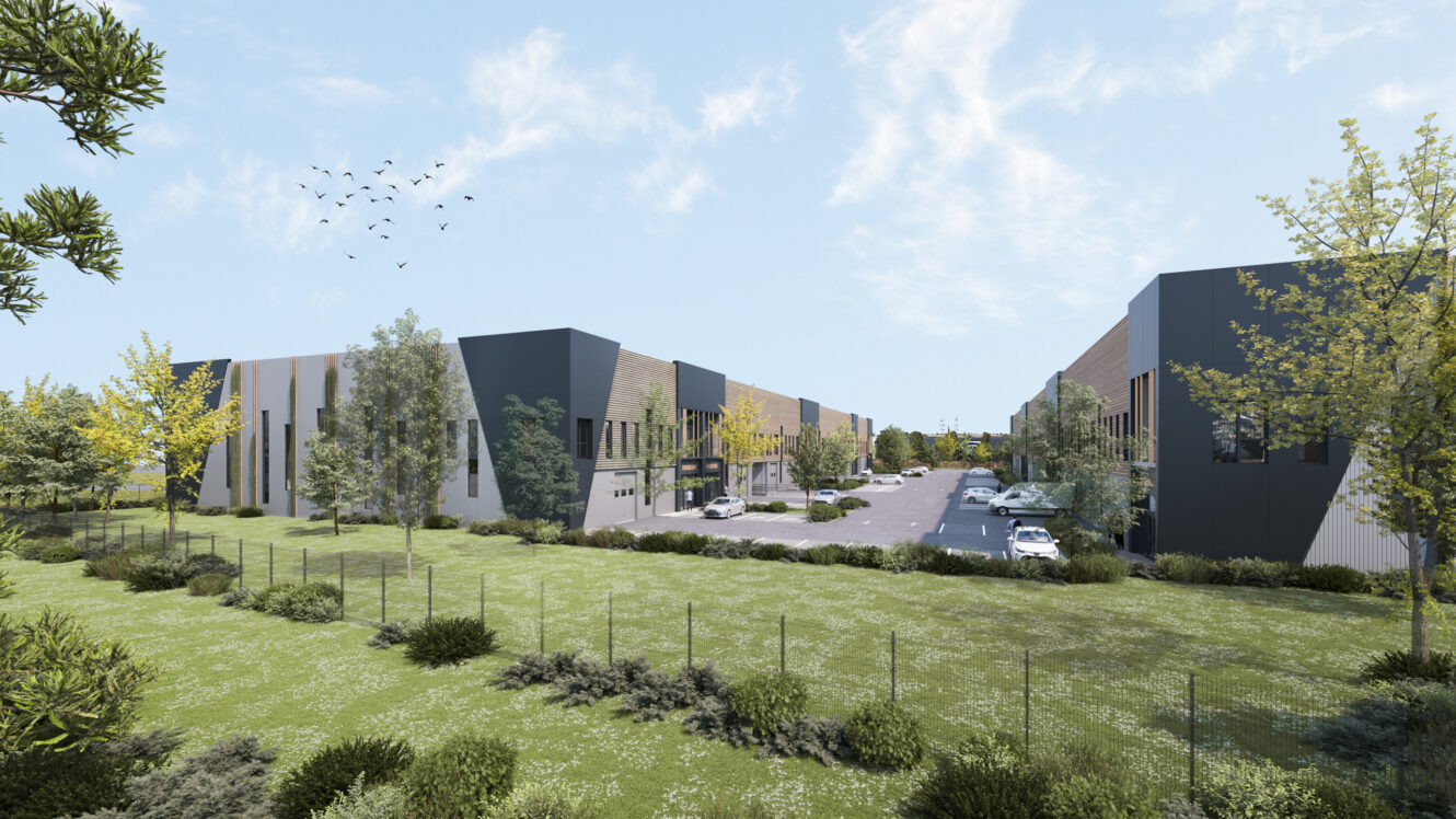 Bâtiments industriels modernes avec parking et plusieurs voitures garées, entourés d'herbe verte, d'arbres et d'un ciel clair avec des oiseaux en vol.