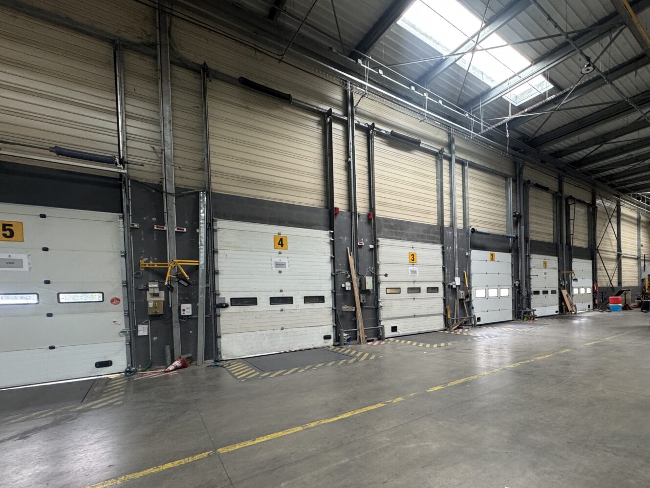 Vue large de l'intérieur d'un entrepôt montrant plusieurs portes de quai de chargement, chacune numérotée, avec des marquages de sécurité sur le sol en béton.