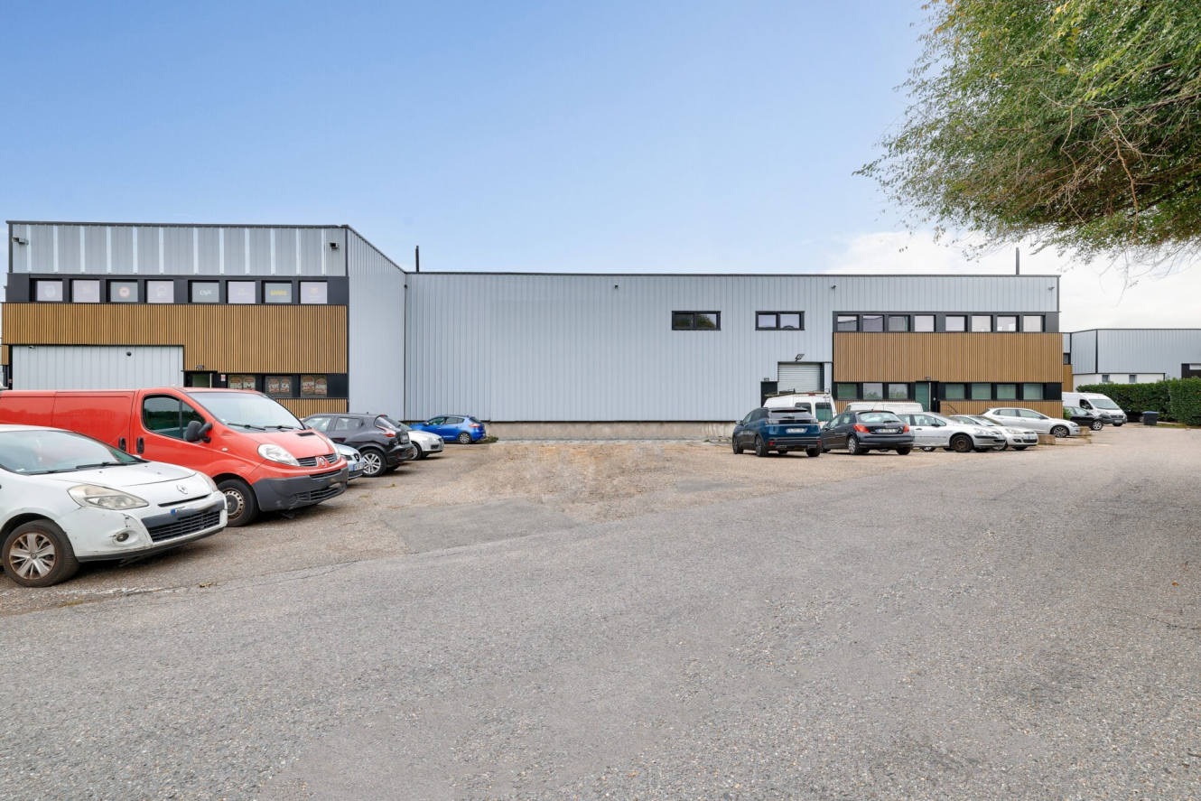 Une rangée de voitures garées devant un grand entrepôt industriel aux panneaux blancs et bruns par temps clair.
