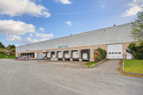 Un grand entrepôt avec plusieurs quais de chargement et un panneau RECEPTION au-dessus de la zone centrale, sous un ciel partiellement nuageux.