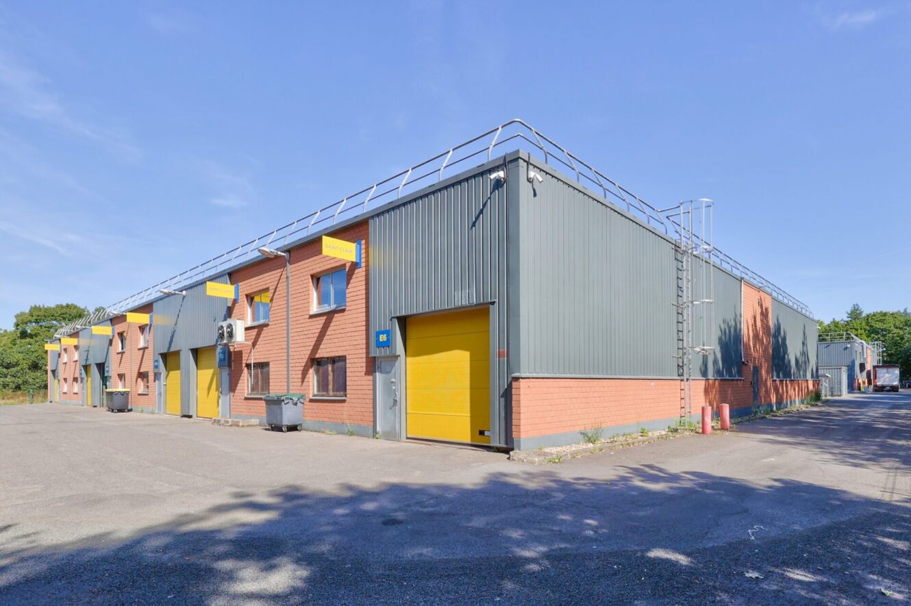 Bâtiment industriel à l'extérieur en brique et métal, avec plusieurs portes roulantes jaunes, situé sur un terrain pavé sous un ciel bleu clair.