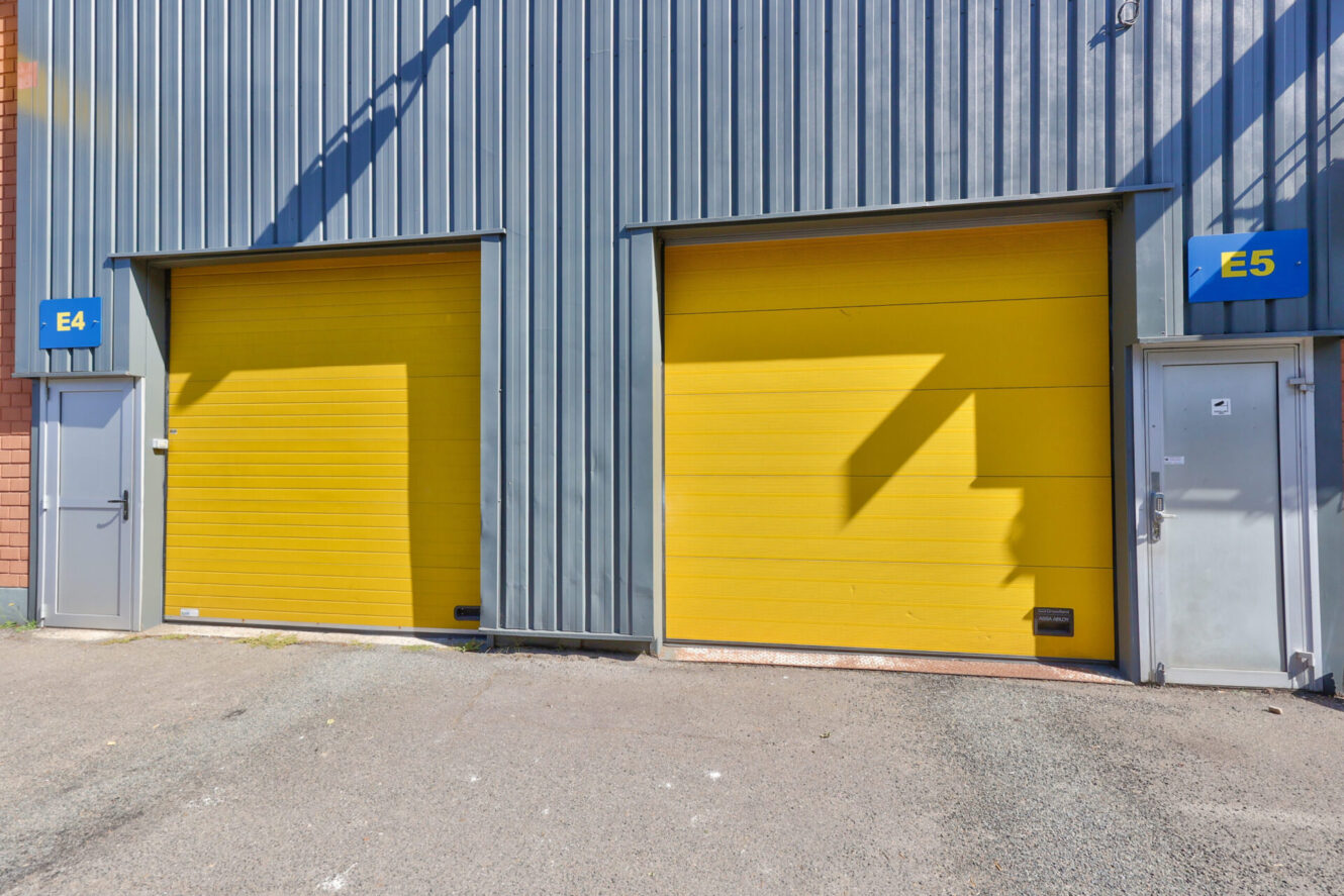 Deux portes de garage industrielles jaunes, étiquetées E4 et E5, se trouvent dans un bâtiment métallique gris, chacune avec une petite porte d'entrée à côté.