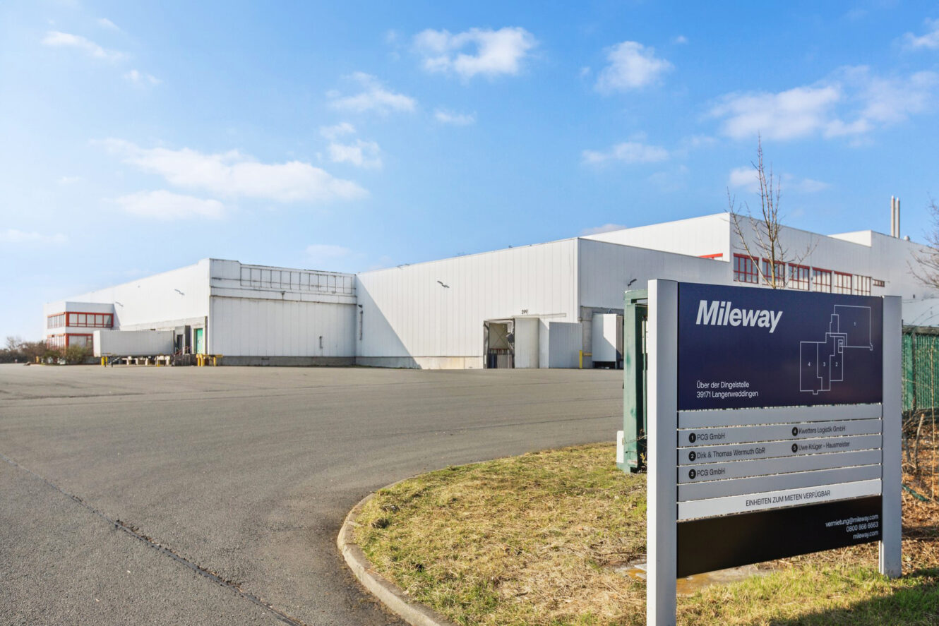 Ein großes weißes Industrielager mit einem Mileway-Schild im Vordergrund unter einem klaren blauen Himmel.