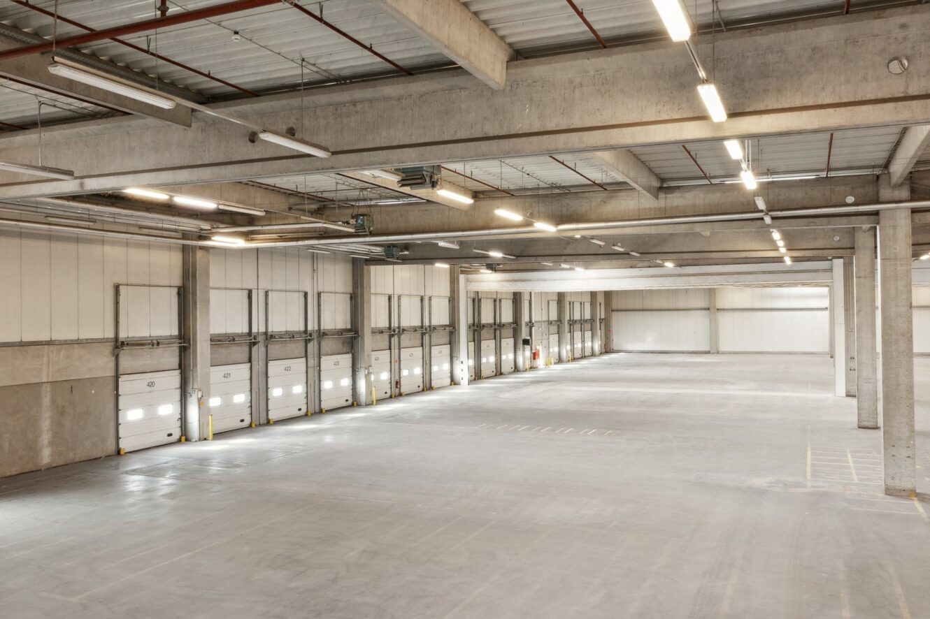 Geräumiges, leeres Lagerhaus mit Betonböden, hohen Decken und mehreren Ladetoren an einer Wand.