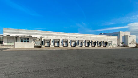 Ein großes Industrielager mit mehreren Laderampen und geschlossenen Hallentoren vor einem strahlend blauen Himmel.