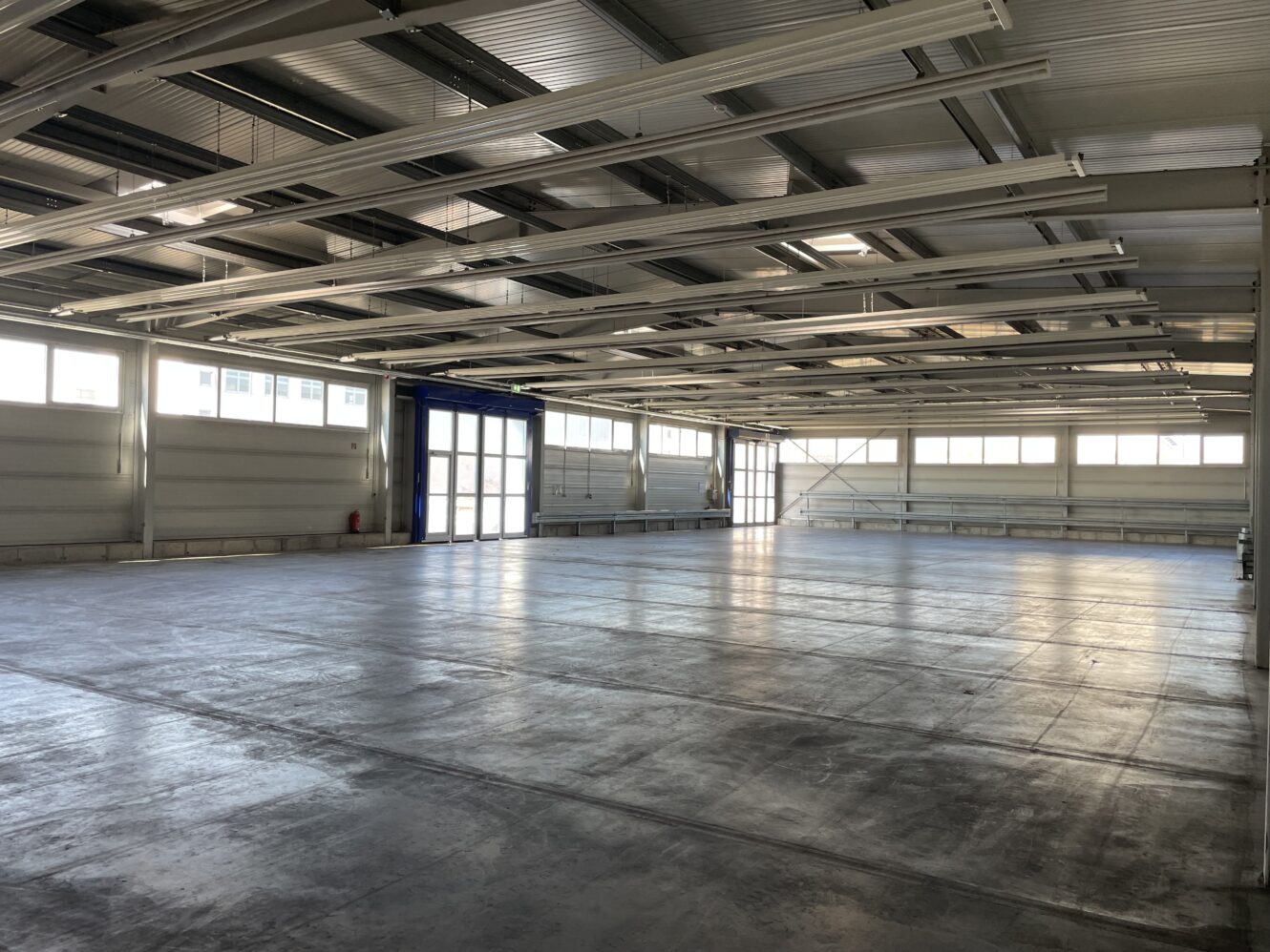 Das Innere eines leeren Industrielagers mit Betonböden, weißen Wänden, großen Fenstern und Oberlichtstrukturen.