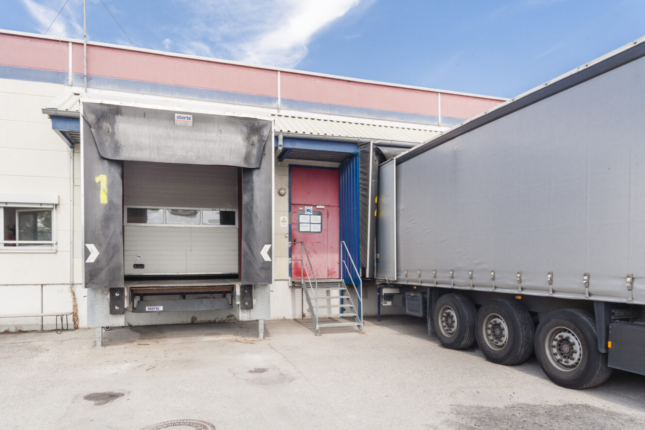 Eine Laderampe mit einem geschlossenen Sektionaltor und einer Treppe neben einem geparkten Lastwagen in einem Industriegebäude.