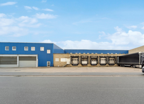 Ein Lagerhaus mit blauer Fassade, geschlossenen Ladetoren und einem geparkten Sattelschlepper vor dem Gebäude bei klarem Himmel.