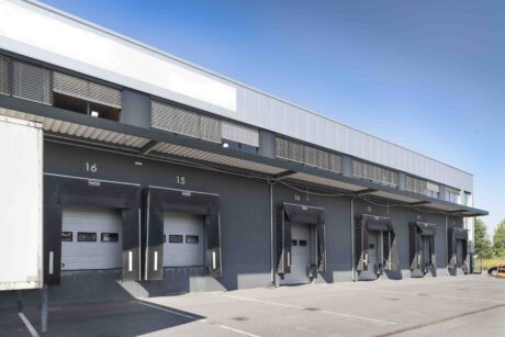 Eine Reihe von Verladetoren mit den Nummern 13 bis 16 an einem modernen industriellen Lagergebäude mit einem leeren Parkplatz davor.