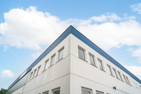 Eckansicht eines modernen weißen Gebäudes mit rechteckigen Fenstern unter einem blauen Himmel mit vereinzelten Wolken.