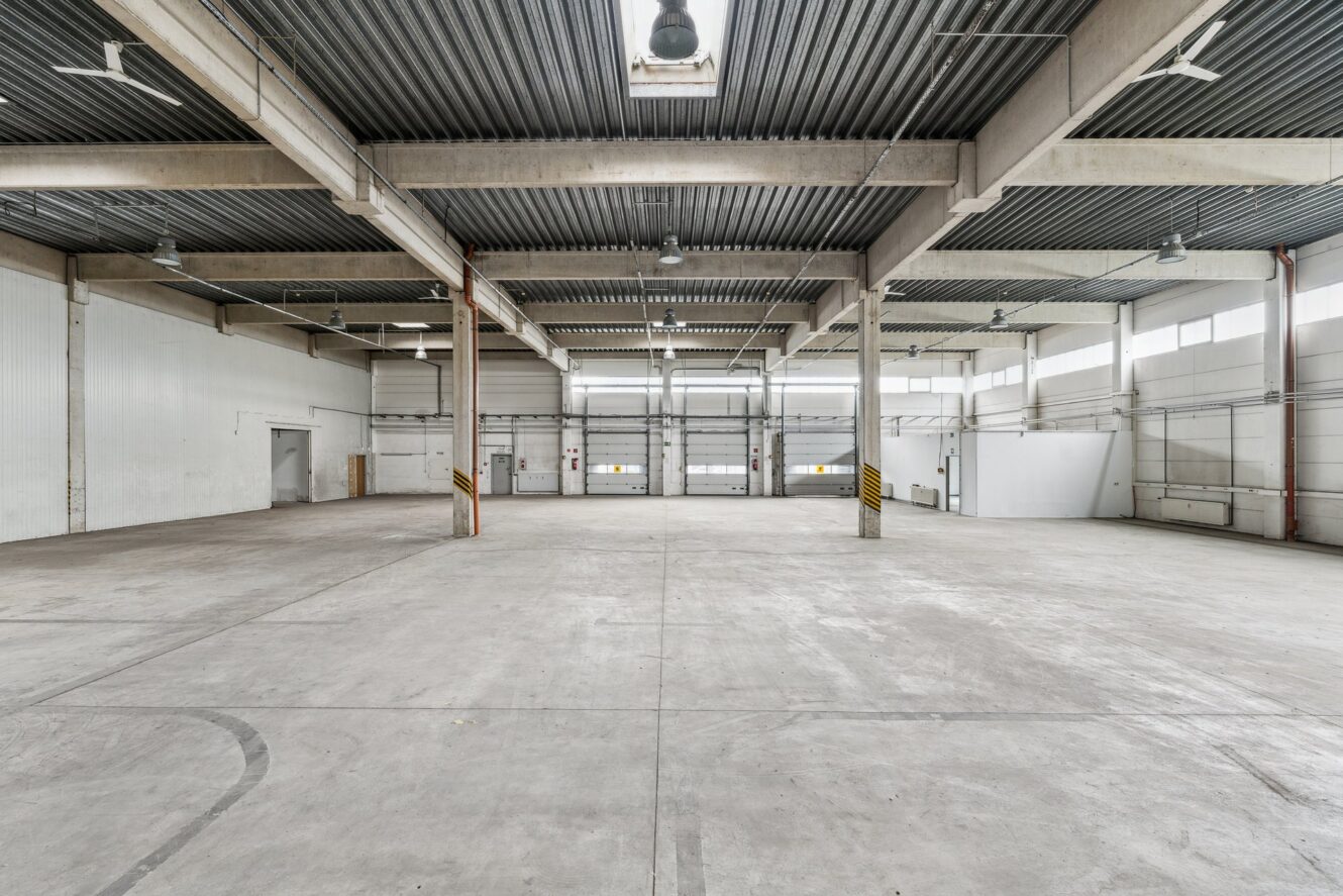 Leeres Industrielager mit Betonböden, hohen Decken, großen Fenstern und Metallträgern; der Raum ist durch Oberlichter und Oberlichter gut beleuchtet.