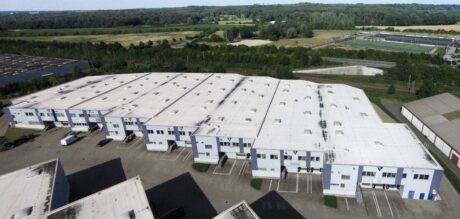 Luftaufnahme eines großen, weiß gedeckten Industrielagerkomplexes mit Verladedocks, umgeben von Feldern und Bäumen.