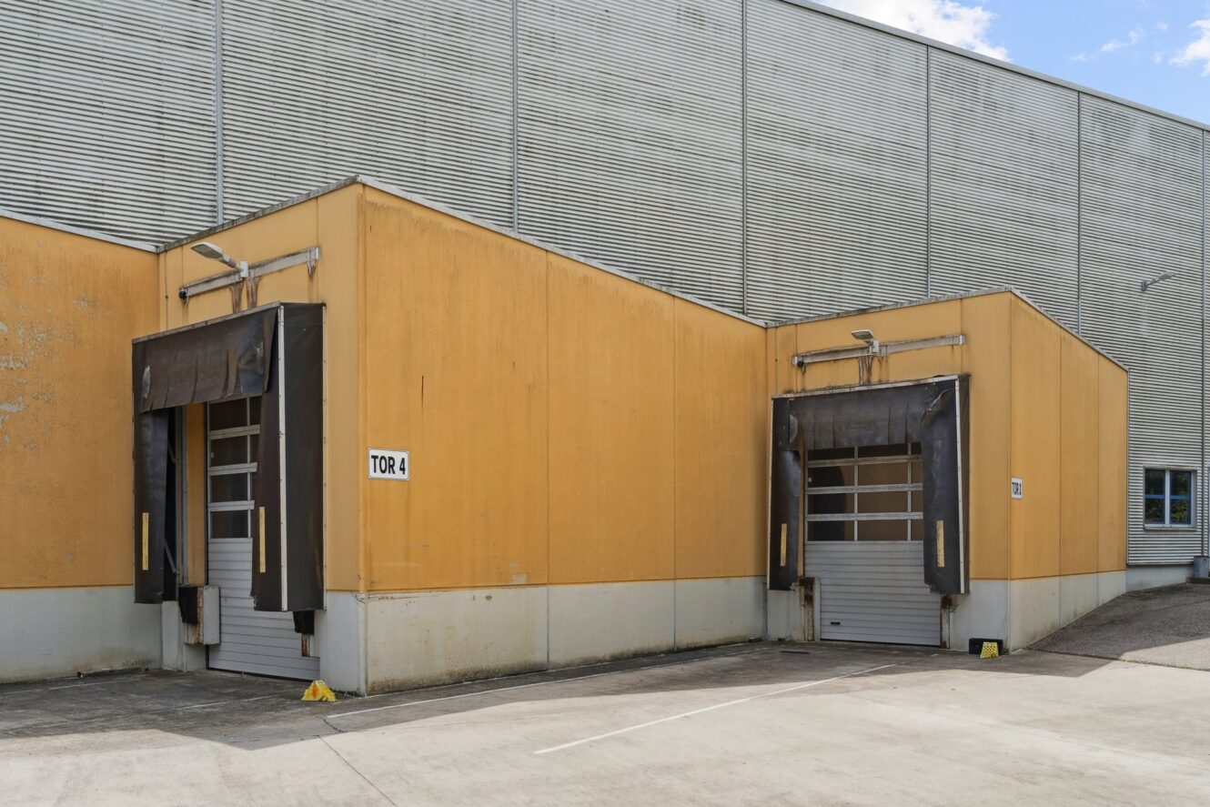 Zwei gelbe Laderampen mit teilweise geschlossenen Rolltoren an einem Industriegebäude; eine trägt die Aufschrift „Tor 4“ und der Bereich ist leer.