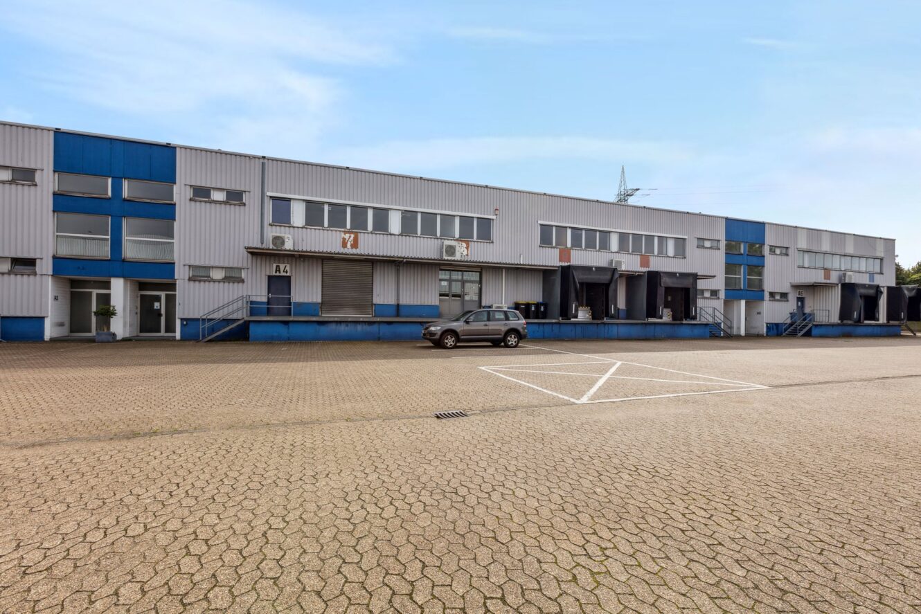 Ein großes industrielles Lagergebäude mit blauem und grauem Äußeren, mehreren Laderampen und einem einzigen geparkten Auto auf dem Vorplatz.