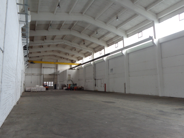 Großes leeres Lagerhaus mit weißen Wänden, hoher gewölbter Decke, Betonboden und minimaler Ausstattung im hinteren Teil.