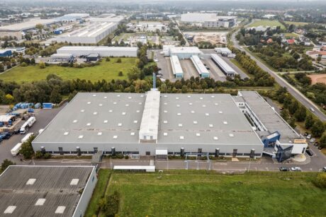 Luftaufnahme eines großen industriellen Lagerkomplexes, umgeben von Straßen, Bäumen und anderen Gebäuden in einem halbstädtischen Gebiet.