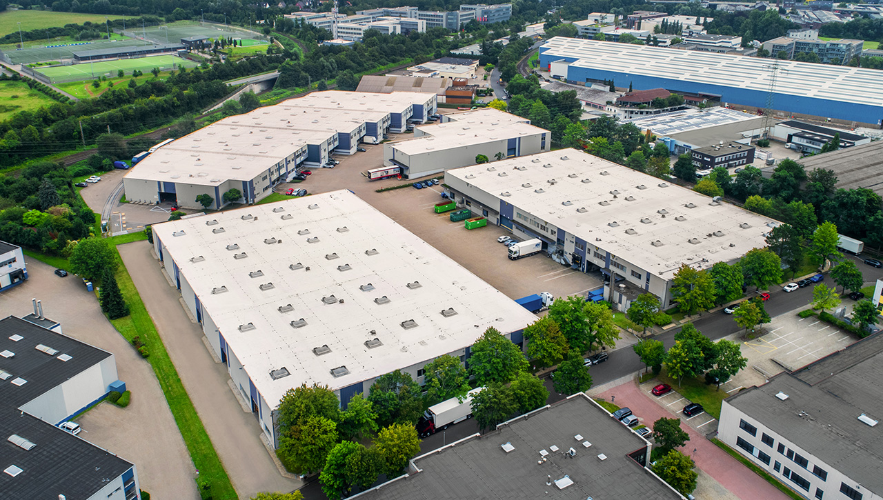 Luftaufnahme eines Industriekomplexes mit großen Lagerhallen, Parkplätzen, Lastwagen und üppigen Grünflächen.