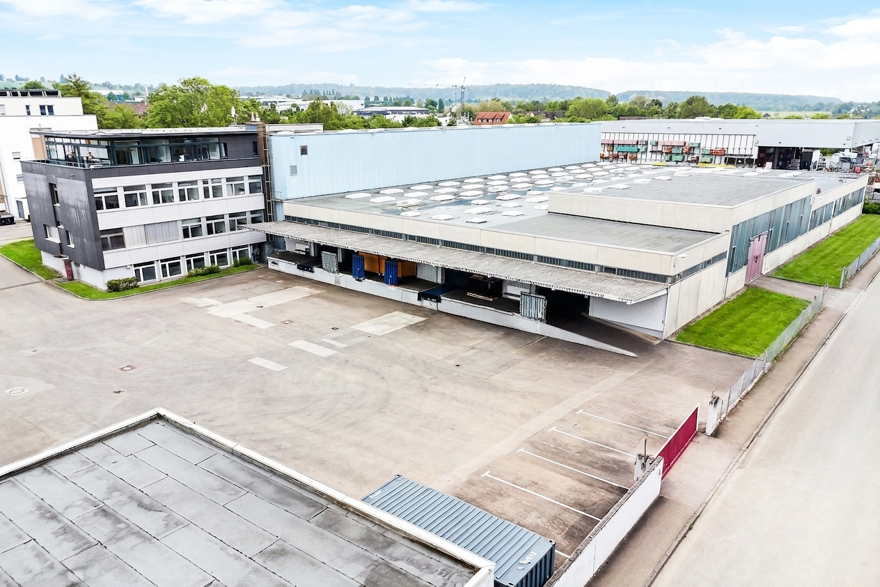 Ein großes Industrielager mit mehreren Laderampen und einem angrenzenden Bürogebäude, umgeben von Gehwegen und Grünstreifen.