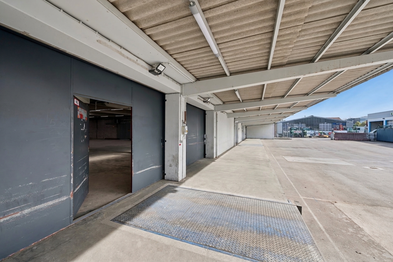 Eine große industrielle Laderampe mit offenen Garagentoren, Betonboden und einer Metallrampe in einem Gewerbegebiet an einem klaren Tag.