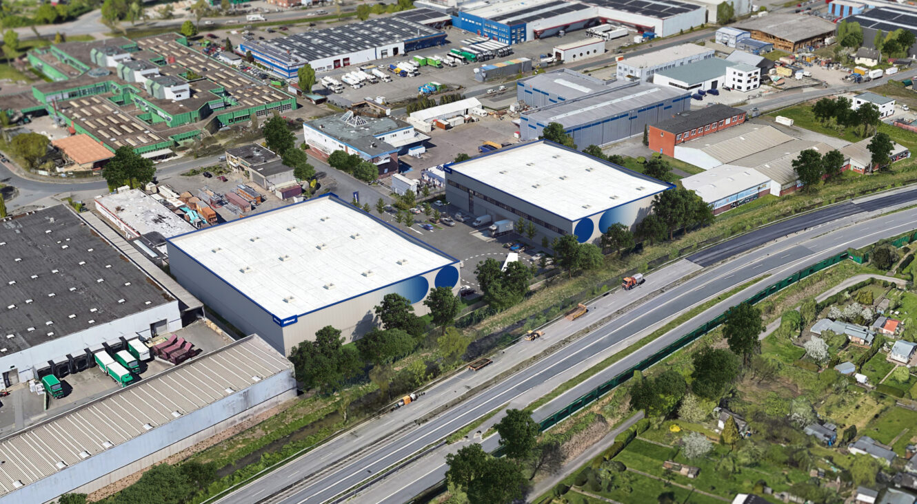 Luftaufnahme von zwei großen Industrielagern mit weißen Dächern und Bäumen um sie herum, in der Nähe einer mehrspurigen Straße in einem Gewerbegebiet.