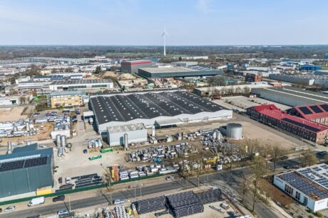 Luftaufnahme eines Industriegebiets mit Lagerhallen, Lagerplätzen, Fabriken und einer Windkraftanlage unter klarem Himmel.