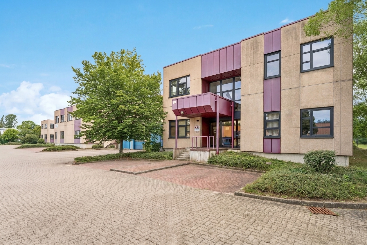 Ein zweistöckiges Geschäftsgebäude mit beigen Wänden, violetten Akzenten und großen Fenstern, umgeben von Bäumen und einem leeren, gepflasterten Parkplatz unter blauem Himmel.