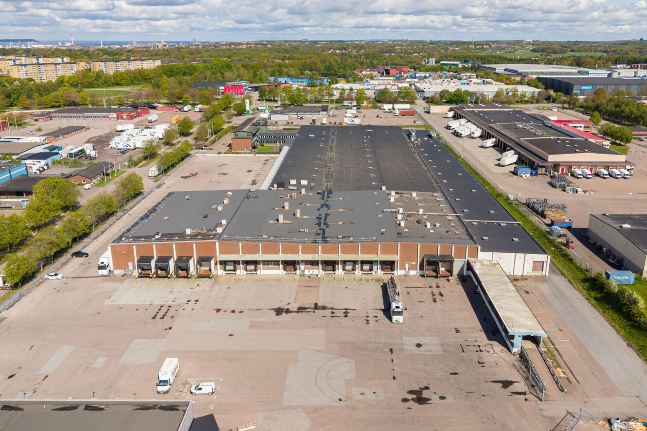 Flygbild över ett stort lager med lastkajer, många lastbilar samt närliggande industribyggnader och vägar.