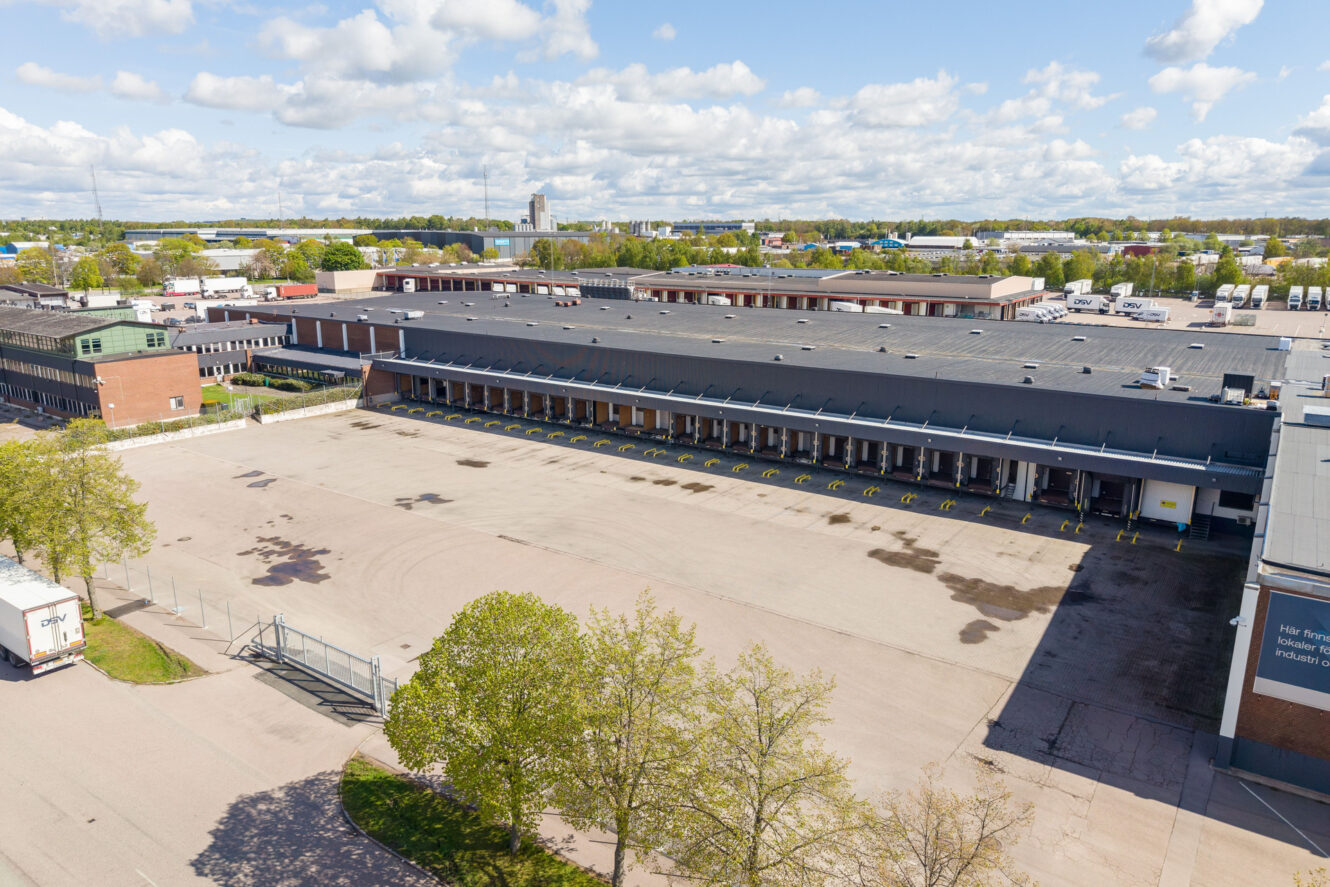 En stor, tom lastkaj vid ett industrilager, där flera lastplatser och utspridda fordon syns under en delvis molnig himmel.