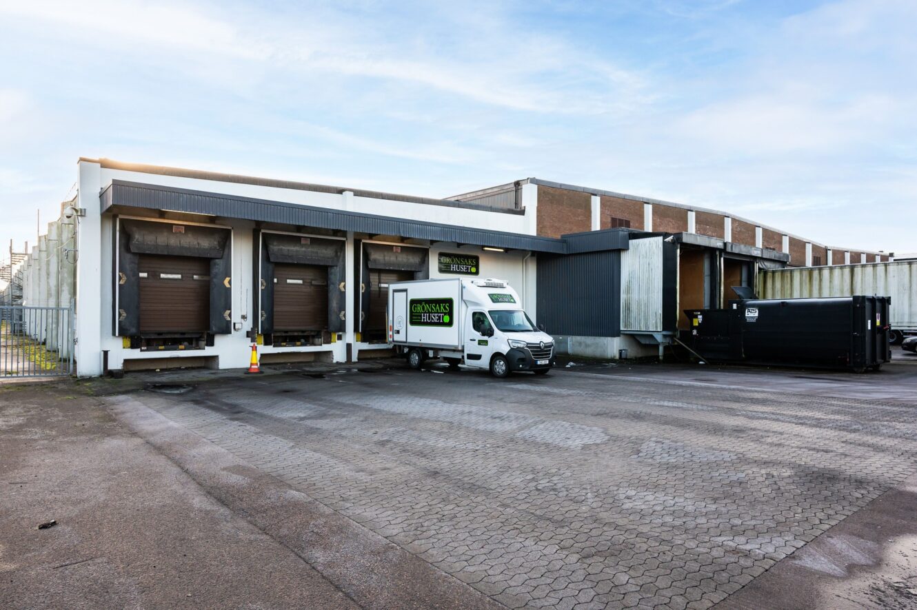 En vit skåpbil står parkerad vid en lastkaj utanför ett stort industrilager med flera stängda lastkajer.