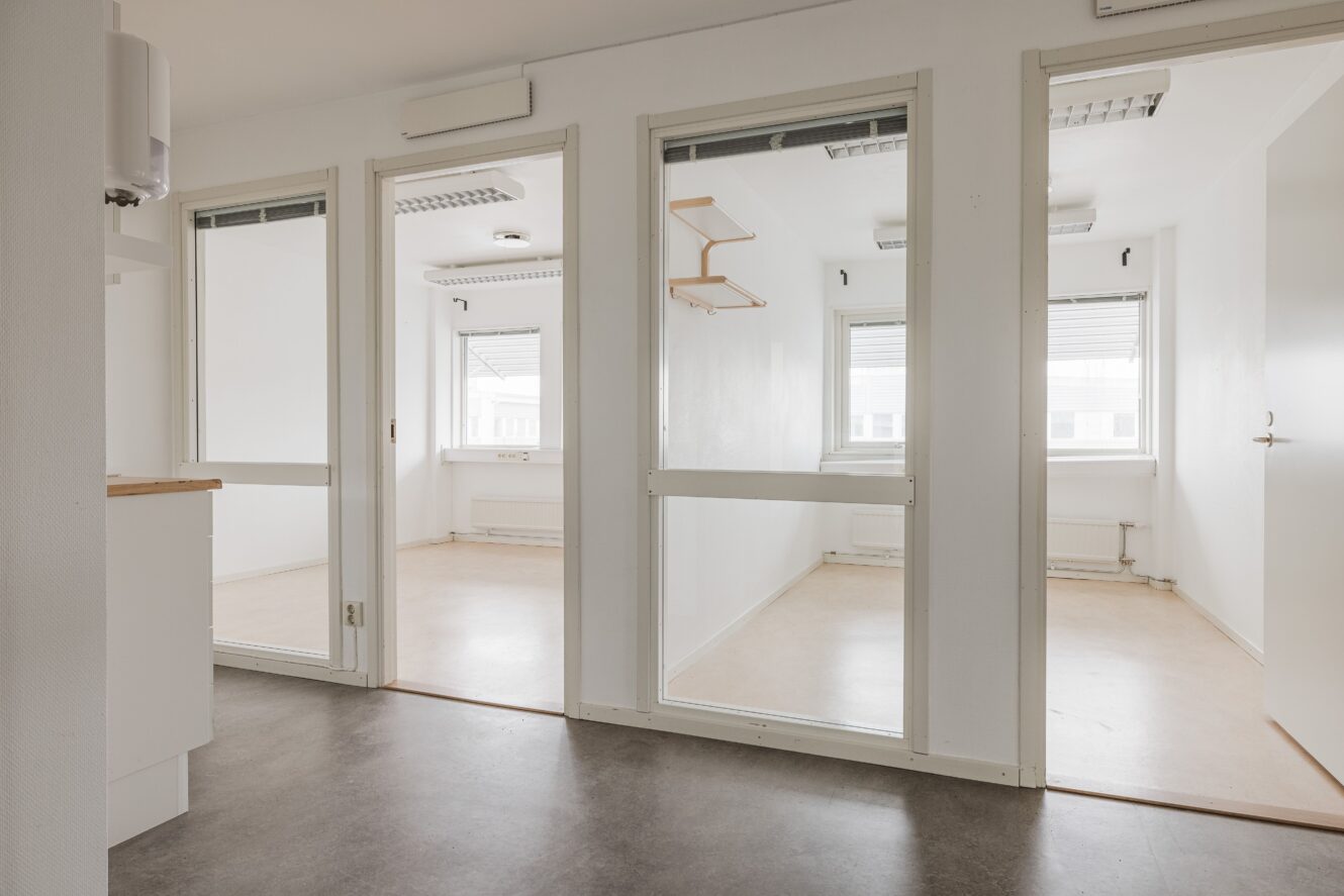 En minimalistisk interiör med tre små rum åtskilda av glasdörrar, vita väggar och stora fönster som släpper in naturligt ljus i varje utrymme.