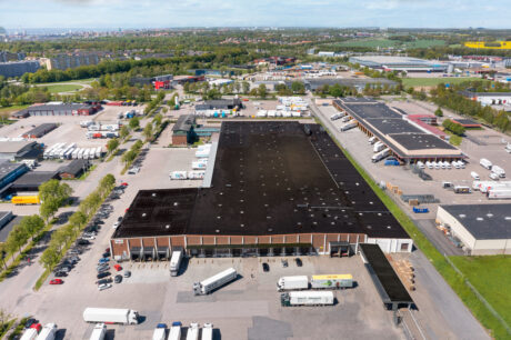 Flygfoto över ett industriellt lagerkomplex med flera lastbilar parkerade runt byggnaden och omgivande lastbryggor.