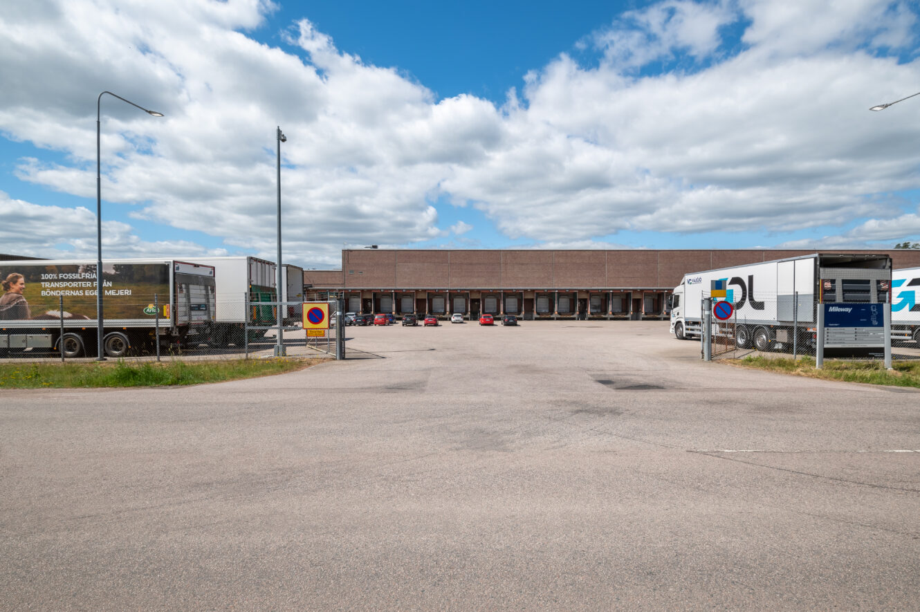 Bred vy över en lastkaj i ett lager med flera lastbilar parkerade i närheten under en delvis molnig himmel.