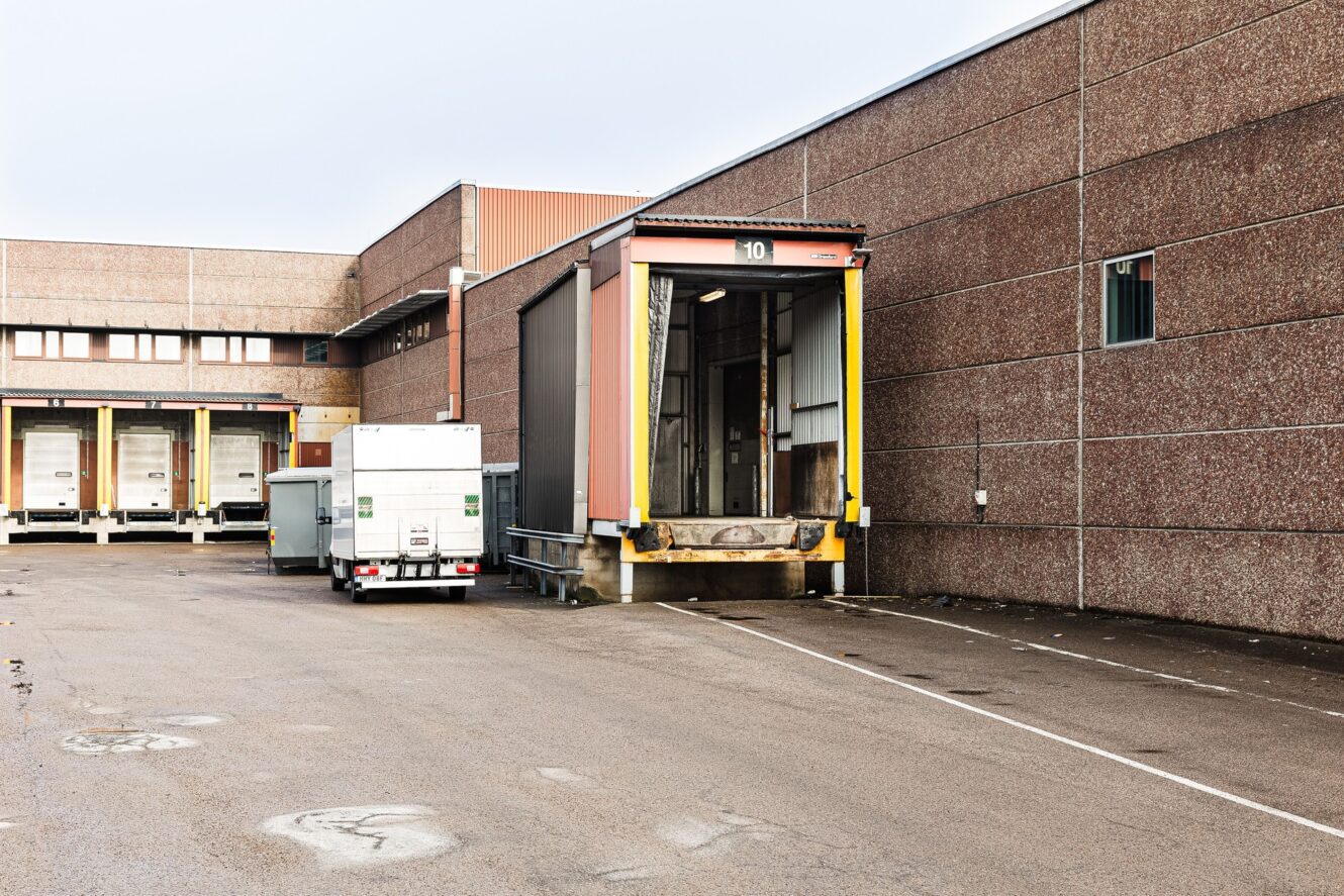 En lastkaj utanför ett lager, med flera lastkajer och en parkerad vit lastbil nära en av lastkajerna.