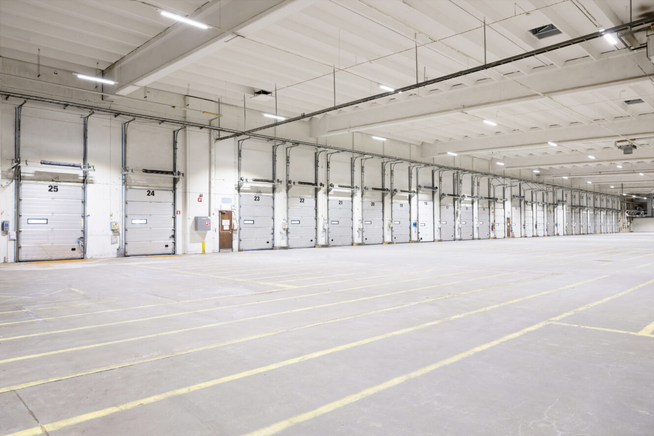 Stor, tom lagerlokal med flera numrerade lastbryggor och målade linjer på betonggolvet.