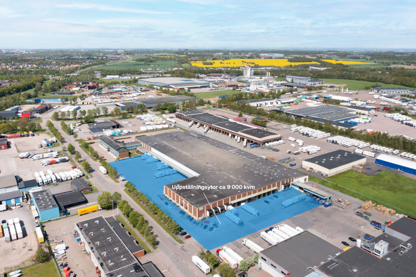 Flygbild över ett industriområde med en stor lagerlokal markerad i blått, märkt Uppställningsytor ca 8 000 kvm, omgiven av lastbilar, vägar och andra byggnader.