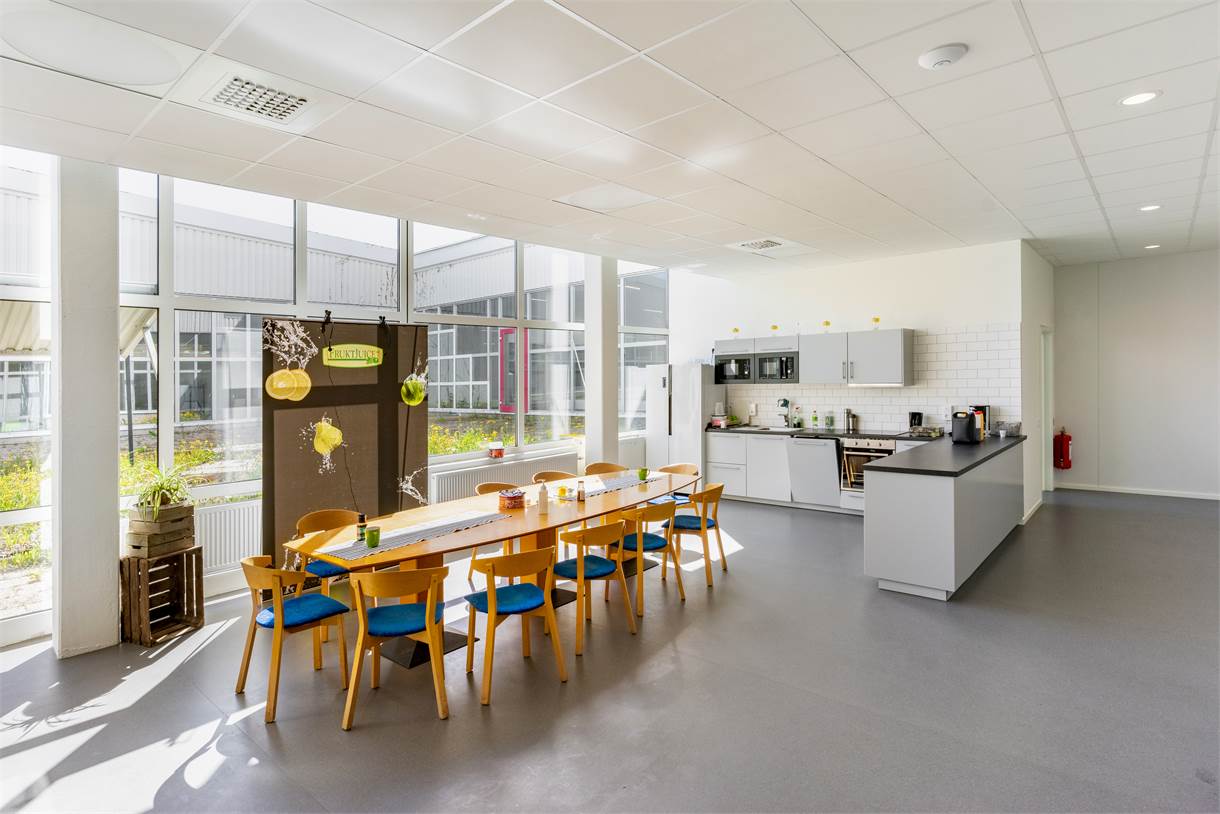 Ljust, modernt kök och matplats med ett långt träbord, åtta stolar, pentry, mikrovågsugn, kaffebryggare och stora fönster som släpper in naturligt ljus.