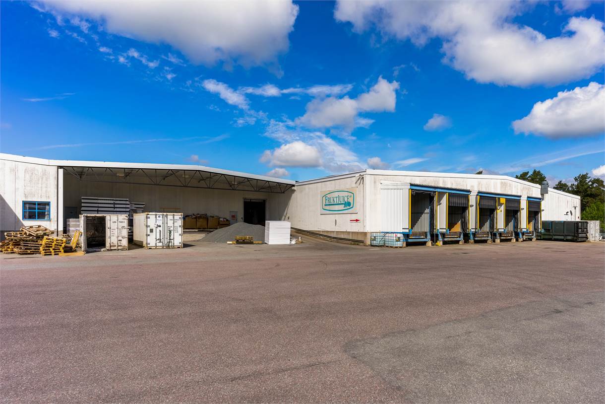 Ett stort industrilager med lastkajer, containrar och lastpallar utomhus under en blå himmel med spridda moln.