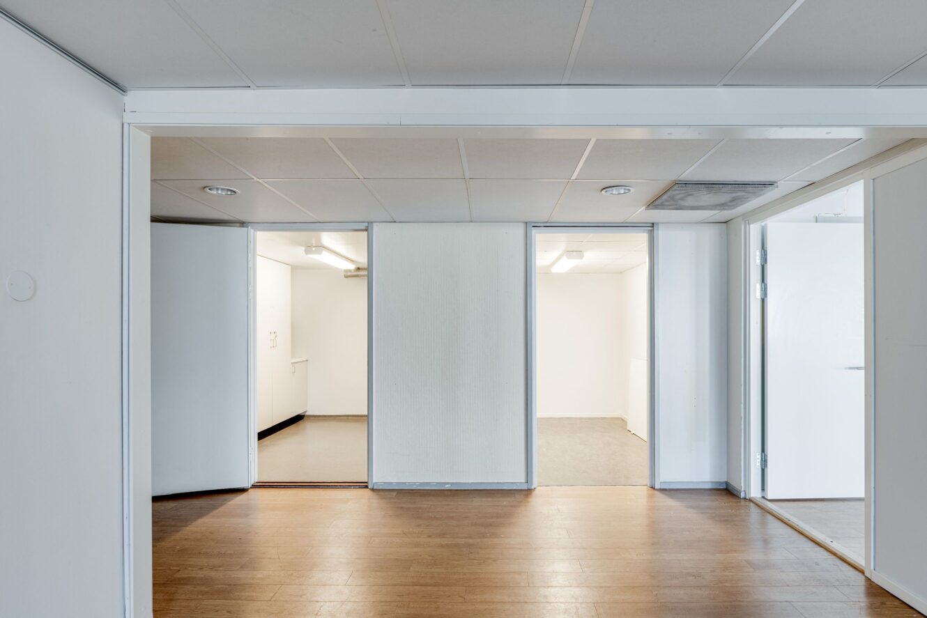 Vy över tre dörröppningar som leder till separata tomma rum med vita väggar, taklampor och trä- eller klinkergolv.