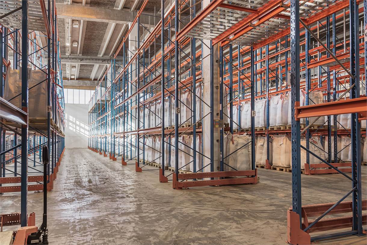Lagerlokal med höga metallhyllor, vissa med stora vita säckar, och en bred tom gång.