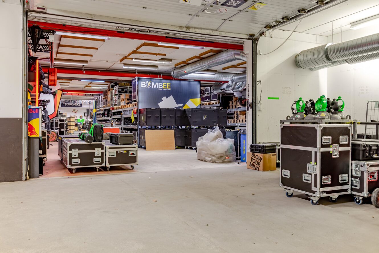 En lagerlokal med organiserade hyllor, stora utrustningslådor, lådor och industriell belysningsutrustning som syns i hela utrymmet.