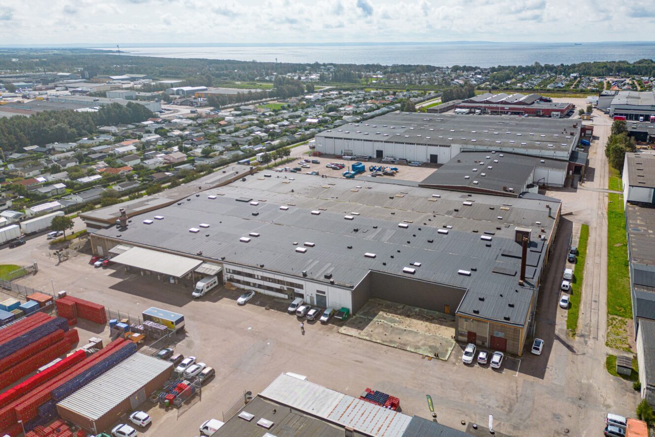 Flygfoto över ett stort industriellt lagerkomplex med närliggande fraktcontainrar, lastbilar och omgivande bostads- och affärshus.