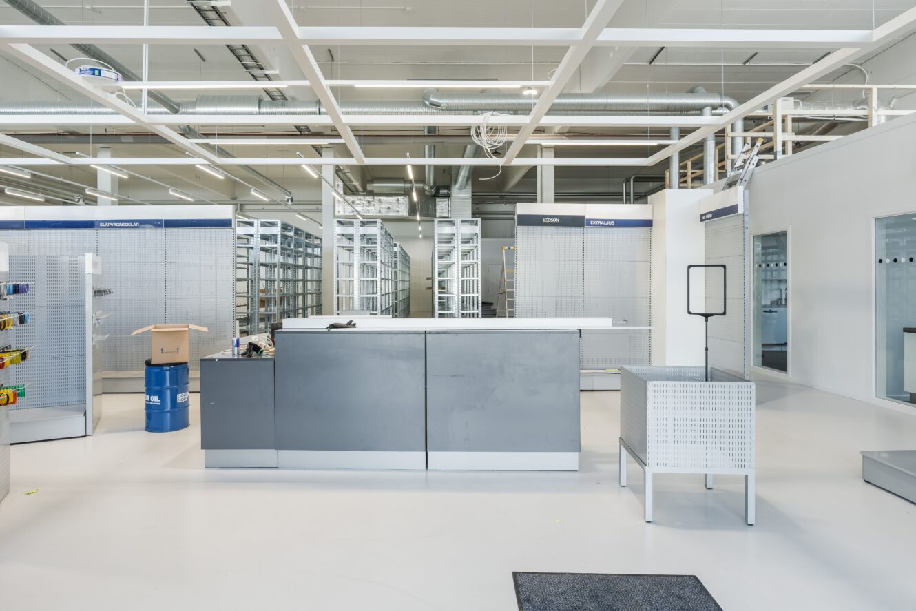 En tom butiksinredning med metallhyllor, en central disk och minimala möbler i starkt ljus.